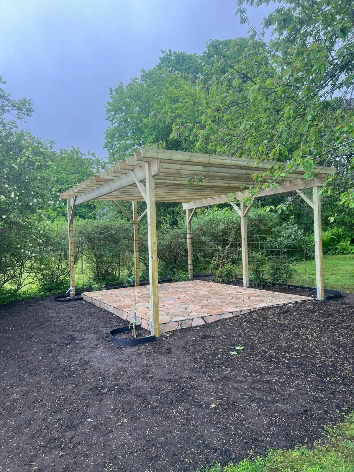Pergola i trä över ett golv av natursten i en nyanlagd rabatt