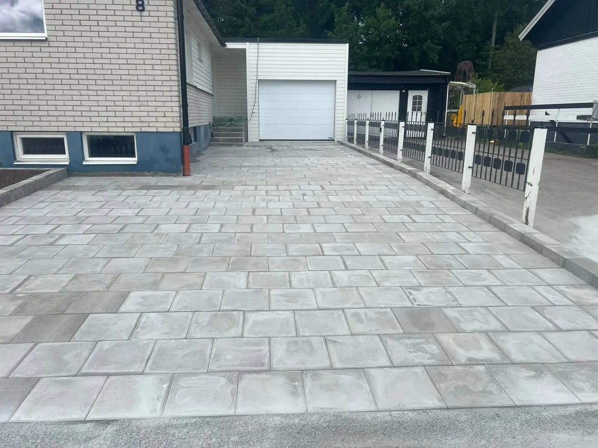 Nylagd uppfart av grå betongplattor fram till ett vitt garage